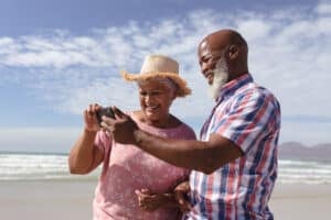 Happy senior african american couple using smartphone at the beach