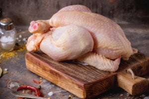 Raw mini Chicken on wooden cutting board with sea salt and different spices over old metal surface